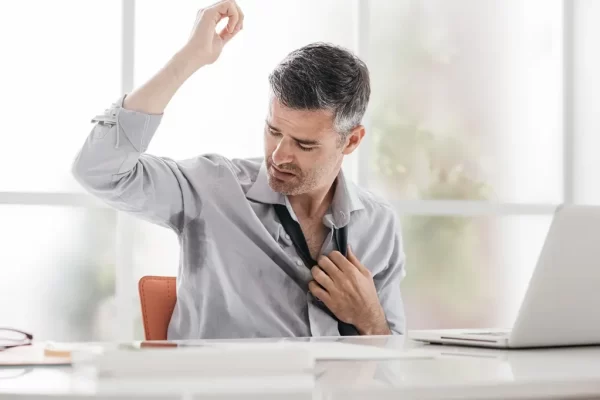 Man at a desk sweating and looking uncomfortable, experiencing hyperhidrosis.